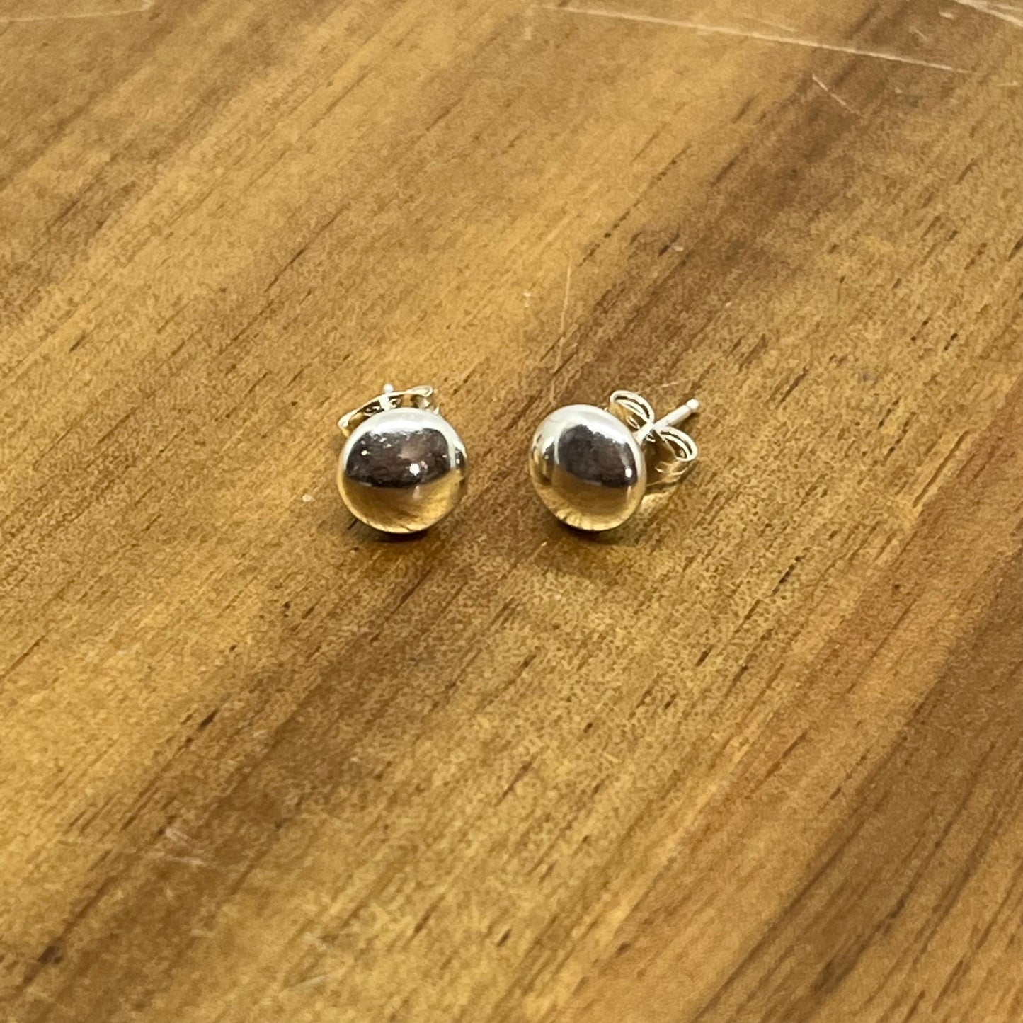 Sterling silver 6.6mm flat head studs displayed on wood.
